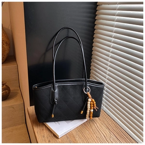 Detail of black quilted shoulder bag featuring a unique wooden bead tassel and soft texture