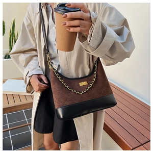 Detail of quilted suede shoulder bag with gold chain strap worn with beige coat