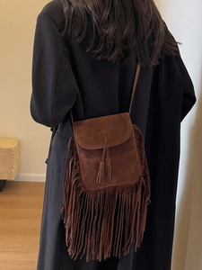 Sac bandoulière en daim marron avec franges porté sur un manteau noir élégant