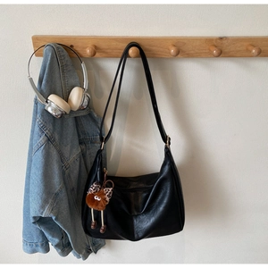 Detail of a black pleated hobo bag with a leopard bow plush charm on a wooden hook