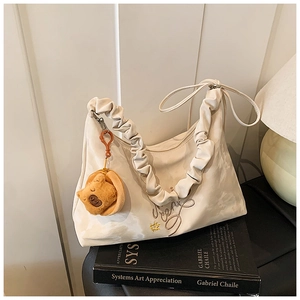 Close-up of cream pleated bag with embroidery and a cute brown bear plush charm