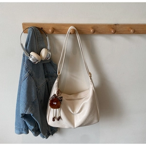 Close-up of cream hobo bag with a plush brown monster pendant on a wooden hook