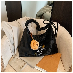 Detail of black pleated hobo bag with white script print and cute bear charm on a chair