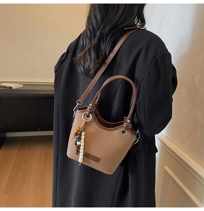 Détail du sac seau en toile avec bordure en cuir marron et pendentif perlé décoratif