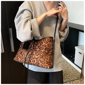On-shoulder view of a retro leopard print tote bag with black faux leather strap detailing
