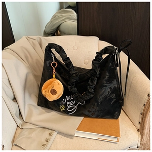 Detail of black nylon pleated shoulder bag with artistic print and cute bear charm