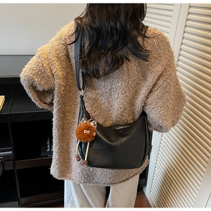 Detail of black faux leather hobo bag with zip closure and cute plush monster pendant