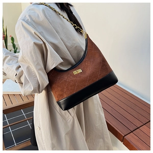 Detail of brown quilted suede dumpling bag with gold chain strap on a model shoulder