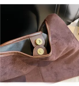 Détail macro de la boucle magnétique dorée sur un sac cabas en daim marron foncé