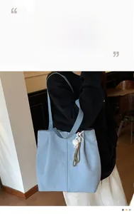 Light blue canvas tote bag with pompom charm and long shoulder strap in a casual style