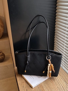 Quilted black shoulder bag with matte finish and wooden bead tassel on a wooden table