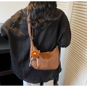 Rear view of model wearing a brown PU leather half-moon shoulder bag with a plush charm