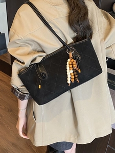Retro black quilted underarm bag with wooden bead fringe shown on a model shoulder
