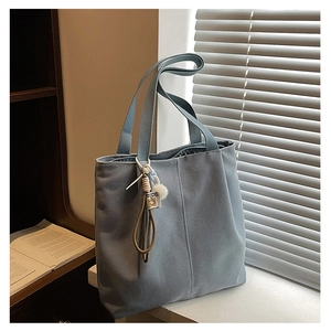Detail of light blue canvas tote bag featuring a white fluffy pompom charm and thick strap