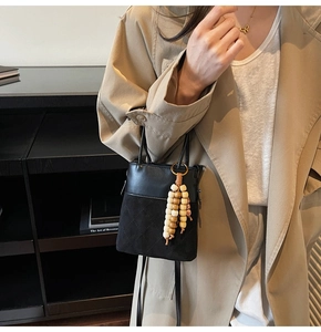 Detail of black suede bucket bag with quilted patterns and colorful wooden beads tassel