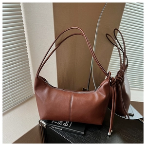 Close-up of brown faux leather half-moon bag with elegant knot and silver ball charm