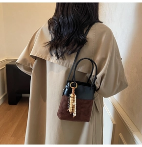 Brown suede and black leather bucket bag shown on a model in a warm interior setting