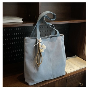 Detail of light blue canvas tote bag featuring thick straps and a plush decorative charm