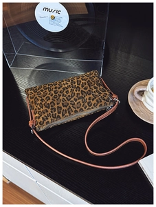 Close-up of leopard print crossbody bag with silver zipper on dark wooden surface