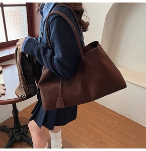 Detail of dark brown matte tote bag with slim shoulder straps worn by model