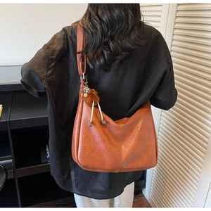 Detail of a brown PU leather hobo bag with leopard print pom-pom charm on a model
