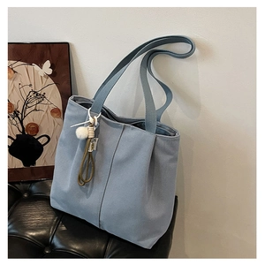 Detail of light blue canvas tote bag with pom-pom charm and shoulder strap on leather seat