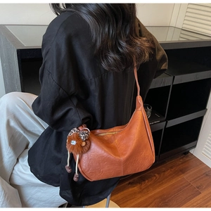 Close-up of caramel half-moon shoulder bag with plush bear charm and leopard bow