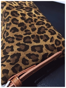 Detail of leopard print faux suede fabric texture and brown leather strap of the handbag