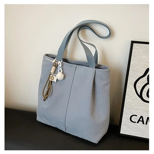 Detail view of light blue canvas tote bag featuring pleat design and plush ball charm