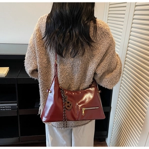 Détail d'un sac à bandoulière en cuir brillant bordeaux avec fermeture éclair en métal