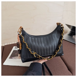 Detail of black woven crescent bag with gold chain and wooden beads on a sofa