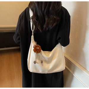 Detail view of large cream hobo bag with a brown plush charm on a black coat model
