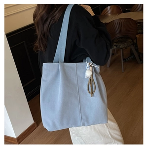 Detail of light blue canvas tote bag with side stitching and soft pompom charm decoration