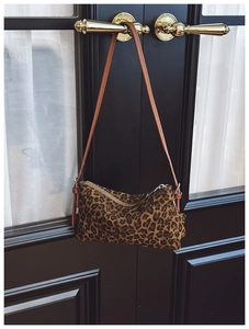 Detail of leopard print crossbody bag with brown strap hanging on a vintage door
