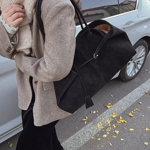 Detail of minimalist black suede tote bag with slim straps worn on shoulder in autumn