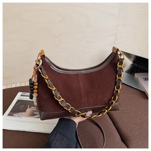 Detailed close-up of dark brown suede hobo bag with gold chain and beaded tassel charm