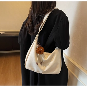 Close-up of off-white dumpling shoulder bag with plush pendant on black blazer