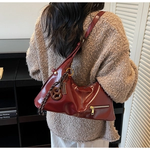 Gros plan sur la texture en cuir bordeaux brillant et les détails dorés du sac hobo