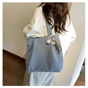 Detail of light blue canvas tote bag with plush ball charm on minimalist model