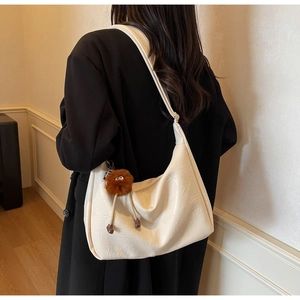 Chic off-white hobo bag with plush charm shown from behind on a model wearing a black coat