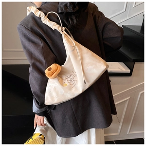Chic off-white hobo bag with pleated strap and bear charm worn with dark blazer