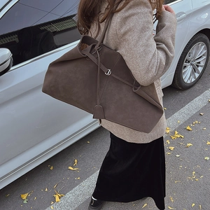 Detail of deep brown suede tote bag with matte texture and metallic rings on shoulder strap