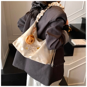 Detail of white satiny hobo bag with pleated strap, blue embroidery, and plush charm