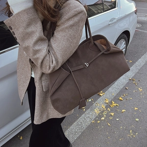 Detail of a large dark brown suede tote bag with adjustable side buckles in outdoor setting
