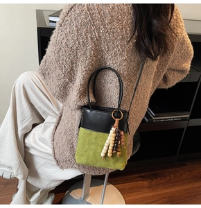 Detail of green suede bucket bag with wood bead tassel and cross-body strap usage