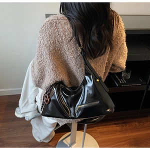 Détail d'un sac hobo noir brillant porté avec un pull en maille marron confortable