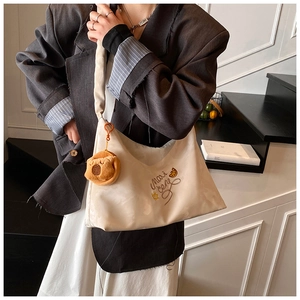 Close-up of beige pleated canvas bag featuring brown embroidery and a cute bear charm