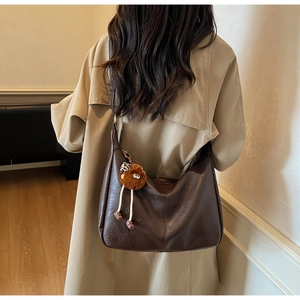 Detail of deep brown leather hobo bag with plush monster charm on model back