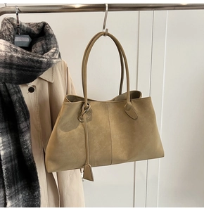 Detail of minimalist khaki suede tote bag hanging on a rack with autumn apparel accessories
