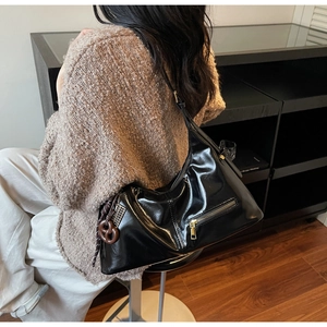 Détail du sac croissant en cuir verni noir avec un charme décoratif en nœud marron